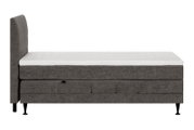 Grijs gestoffeerd eenpersoons boxspringbed met hoog hoofdbord, witte gewatteerde topper en zwarte poten, afgebeeld in zijaanzicht.
