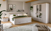 Helles Schlafzimmer-Set in Weiß mit Holz-Akzenten: Doppelbett mit Schublade, Nachttisch und Kleiderschrank mit Spiegeltüren, gezeigt in frontaler Raumansicht aus leicht schräger Perspektive.