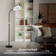 Schwarze LED-Stehleuchte mit rundem Lampenkopf und flexiblem Arm im Wohnzimmer neben weißem Regal und grauem Sofa, Seitenansicht schräg von vorn; Einblendung zur Dimmbarkeit (100% bis ca. 10%)