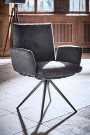 Grauer Armlehnstuhl mit modernem Design, fotografiert aus einem leicht seitlichen Winkel in einem Raum mit Holzwänden und großen Fenstern.