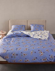 Bettwäsche-Set in Blau mit floralem Muster, bestehend aus Decke und zwei Kissen, auf einem Bett mit beigem Kopfteil, aus der Frontalperspektive fotografiert.