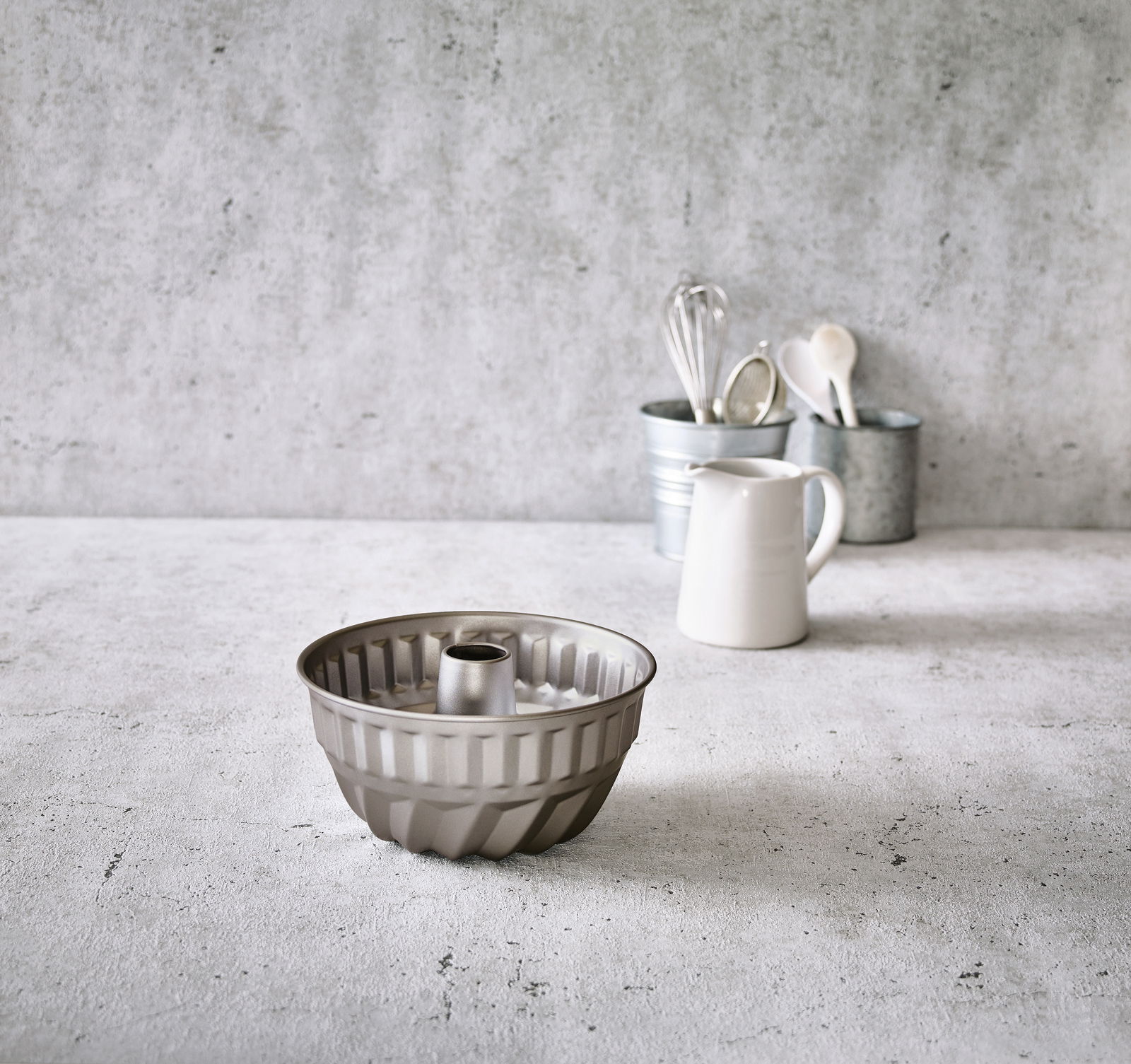 Birkmann Gugelhupfform BASIC BAKING Gugelhupfform aus Metall, frontal auf einem Küchentisch platziert, mit Küchenutensilien im Hintergrund.