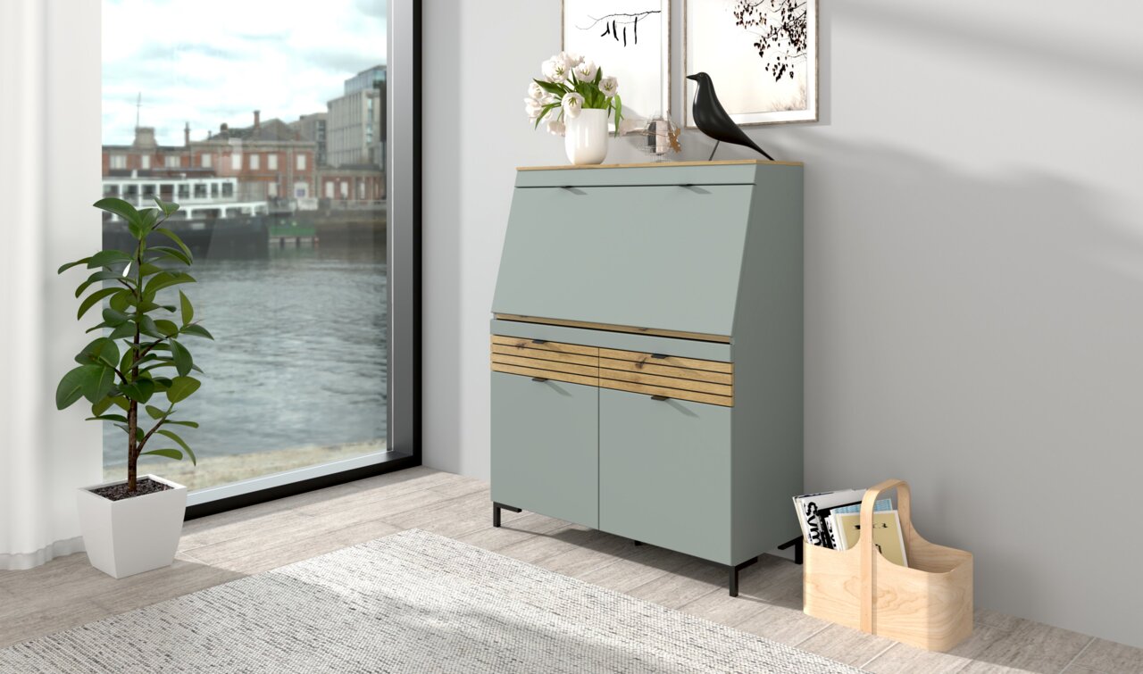 Voleo Sekretär DIANA Moderner Sekretär in einem hellen Raum mit Blick auf ein großes Fenster. Der Sekretär hat eine graue Front mit Holzelementen und steht auf schwarzen Beinen. Auf der Oberseite befinden sich Dekorationen wie eine Vase mit Blumen und eine schwarze Figur. Per