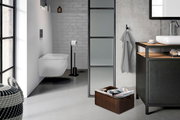 Modernes Badezimmer mit wandhängendem weißen WC, schwarzem Toilettenpapierständer und Waschtisch mit Aufsatzbecken; seitliche Perspektive mit Blick von links in den Raum.