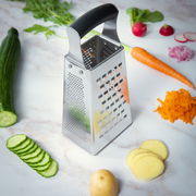 Vierkantreibe aus Edelstahl mit schwarzem Griff, umgeben von geschnittenem Gemüse auf einer Marmoroberfläche, Perspektive von schräg oben.