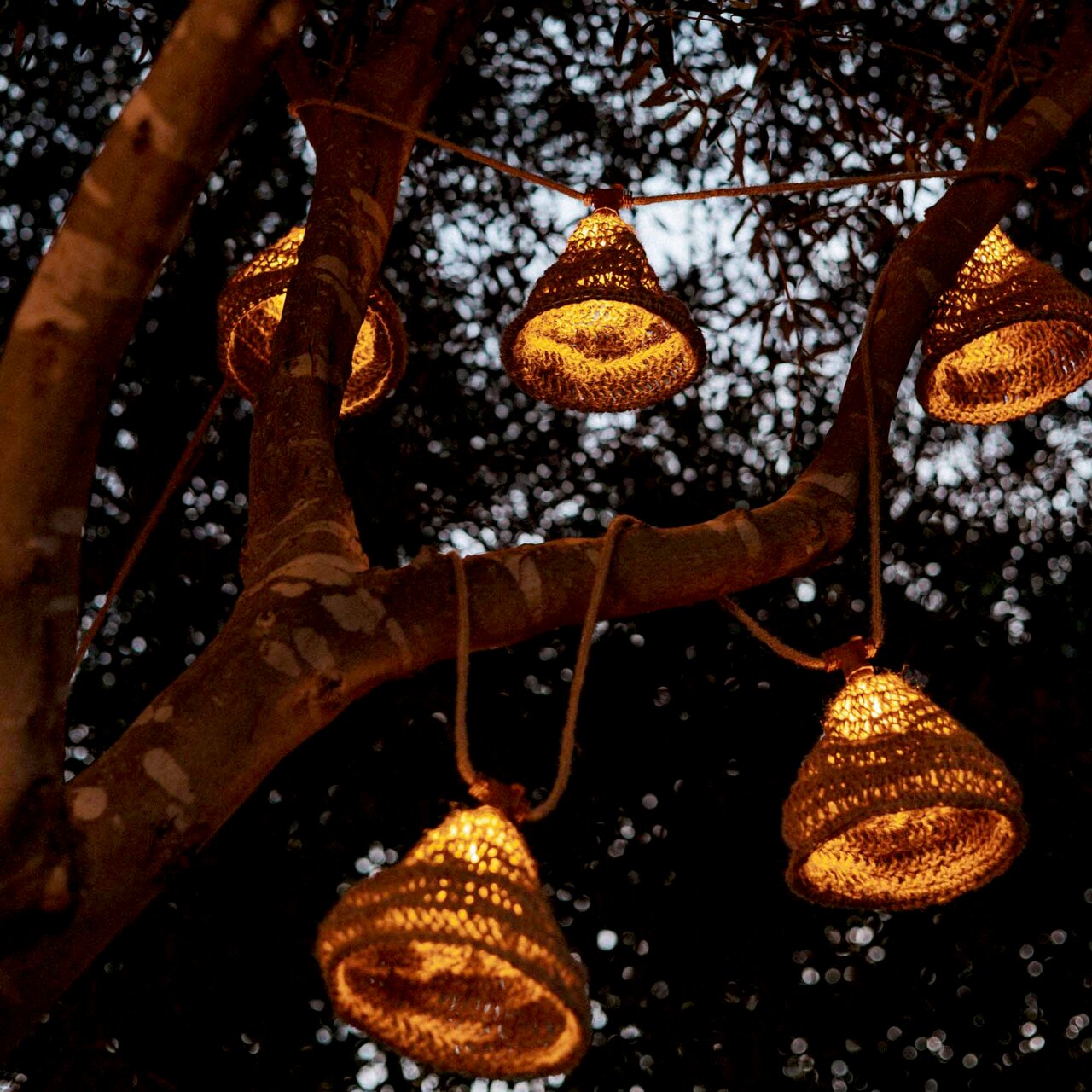 Outdoor-Lichterkette mit solarbetriebenen, warm leuchtenden Lampen in Körben, aufgehängt an einem Baum in der Abenddämmerung, seitliche Perspektive