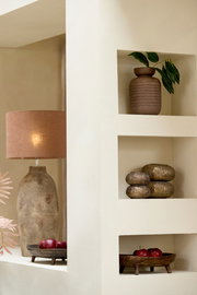 Ein stilvolles Windlicht in einem Regal, umgeben von dekorativen Elementen wie einer Vase mit Blättern und einer Tischlampe. Perspektive von vorne.