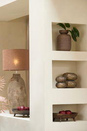 Ein stilvolles Windlicht in einem Regal, umgeben von dekorativen Elementen wie einer Vase mit Blättern und einer Tischlampe. Perspektive von vorne.