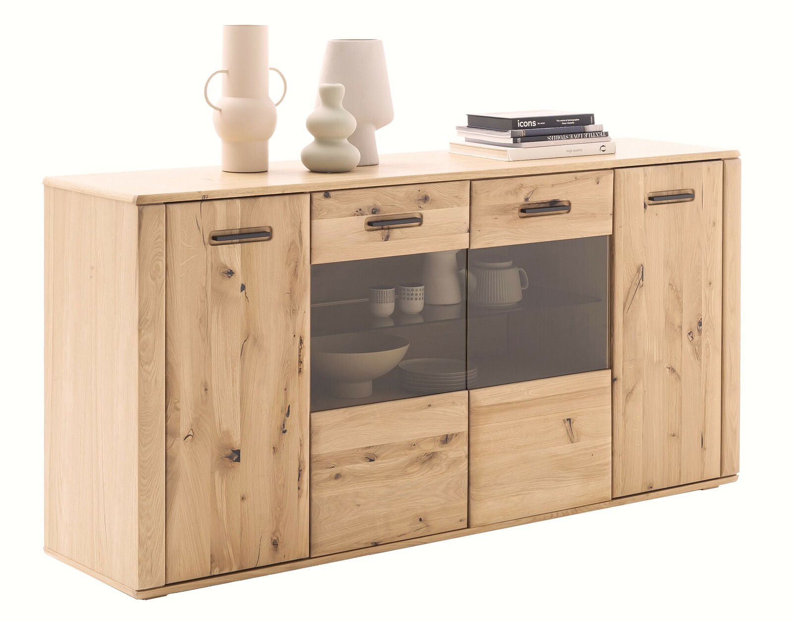 Perspektivische Ansicht eines Cantus Sideboards ASINARA aus hellem Holz mit zwei Türen, zwei Schubladen und einer Glastür in der Mitte, dekoriert mit Vasen und Büchern auf der Oberseite.