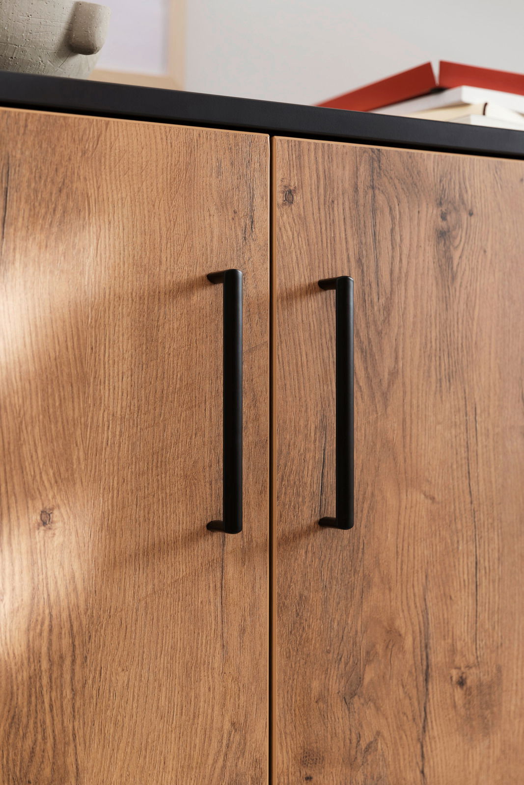 Nahaufnahme eines Schuhschranks mit Holzoptik und schwarzen Griffen, von vorne betrachtet.