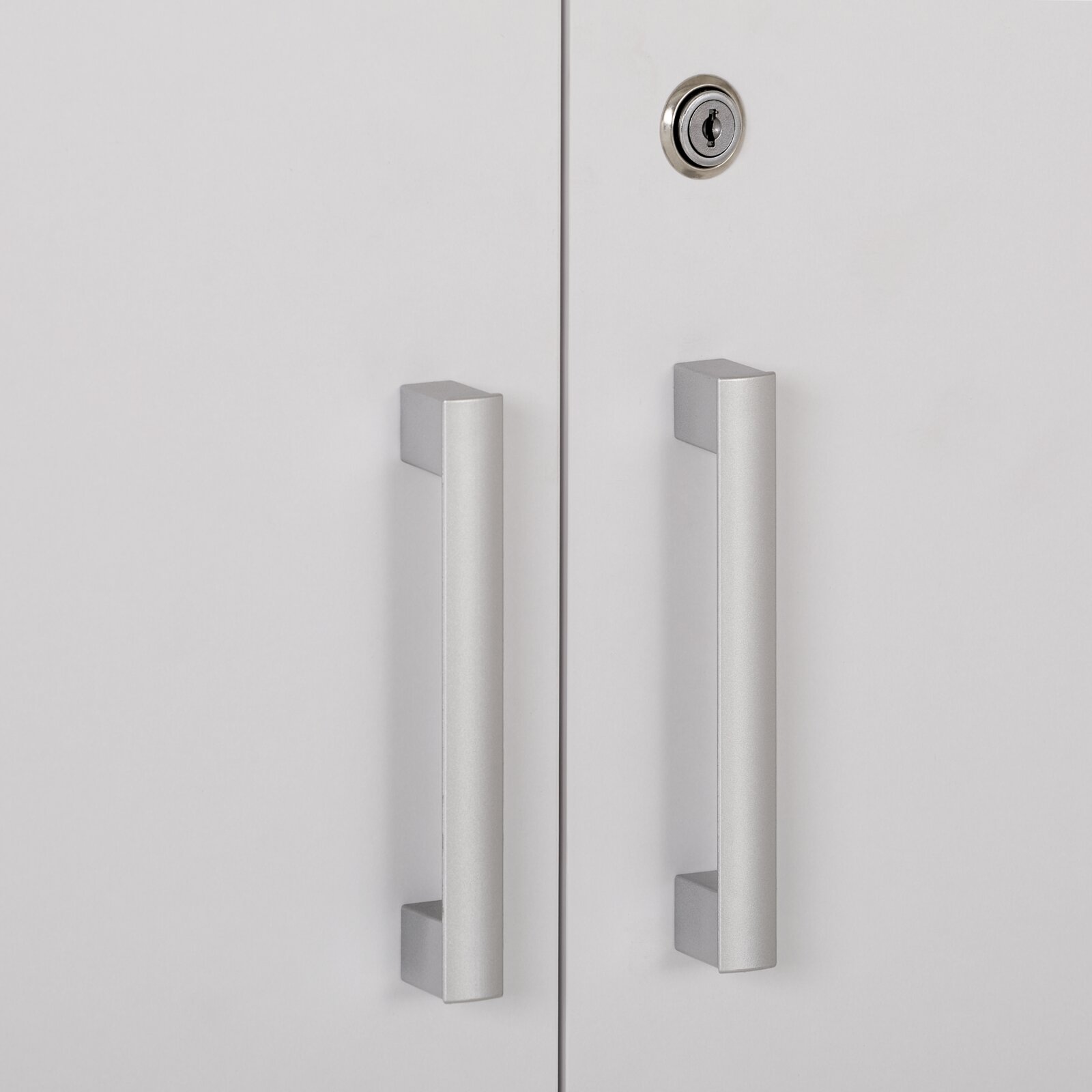 Close-up vooraanzicht van een witte kast met twee lange zilverkleurige handgrepen en een rond cilinderslot op de rechterdeur