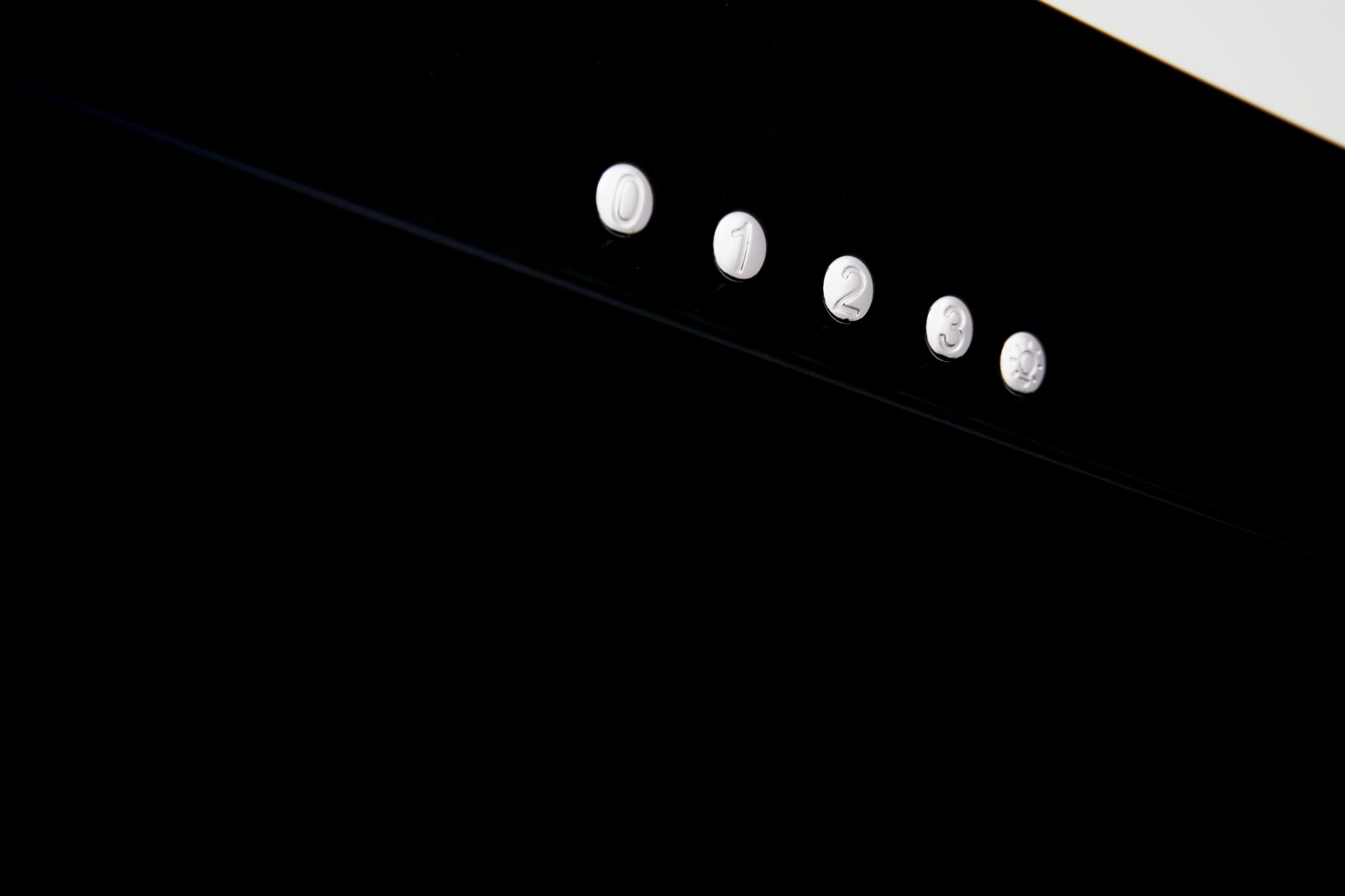 Nahaufnahme von schwarzen Bedienknöpfen mit den Zahlen 0 bis 3 und einem Lichtsymbol auf einer schwarzen Oberfläche, seitliche Perspektive.