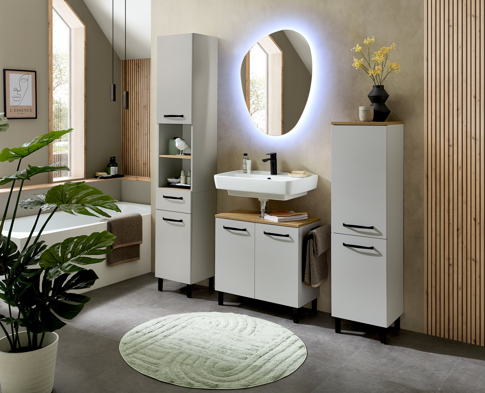 Frontalansicht eines modernen Badezimmers mit weißem Badmöbel-Set (Hochschrank, Waschtischunterschrank und Seitenschrank) mit Holzoptik-Ablagen, ovalem LED-Spiegel und schwarzer Armatur.