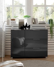 Moderne schwarze Kommode mit Hochglanzoberfläche, frontal fotografiert, dekoriert mit Pflanzen und Büchern vor einem Fenster.