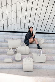 Frau sitzt auf Treppe mit verschiedenen Taschen in Herringbone-Muster, frontale Perspektive