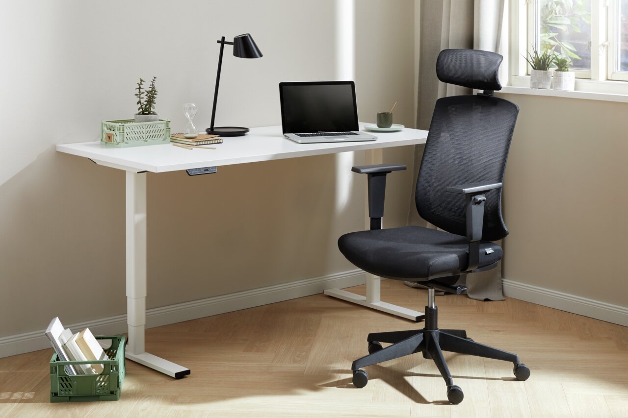 Moderner schwarzer Drehstuhl mit Kopfstütze und Armlehnen, seitliche Perspektive, neben einem weißen Schreibtisch in einem hellen Raum.