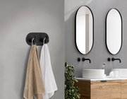 Schwarzer Edelstahl-Doppelhaken an der Wand, frontal betrachtet, mit zwei aufgehängten Handtüchern in einem modernen Badezimmer.