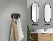 Schwarzer Edelstahl-Doppelhaken an der Wand, frontal betrachtet, mit zwei aufgehängten Handtüchern in einem modernen Badezimmer.