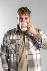 Mann in kariertem Hemd hält eine Tasse mit der Aufschrift 'Coffee FIRST' in der Hand, frontal aufgenommen.