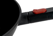 Nahaufnahme eines Guss-Woks mit abnehmbarem Griff und rotem Knopf, seitliche Perspektive
