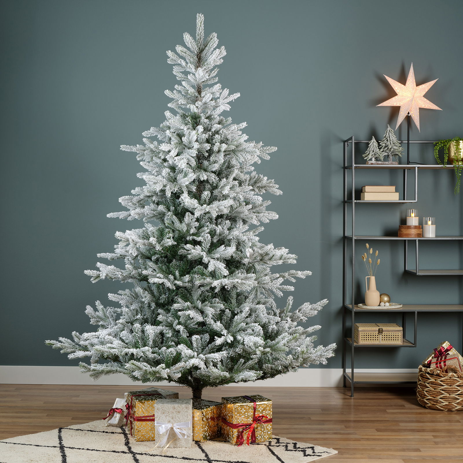 Künstlicher Weihnachtsbaum mit Schnee-Effekt, D.132 H.180 cm, frontal fotografiert, umgeben von Geschenken und weihnachtlicher Dekoration.