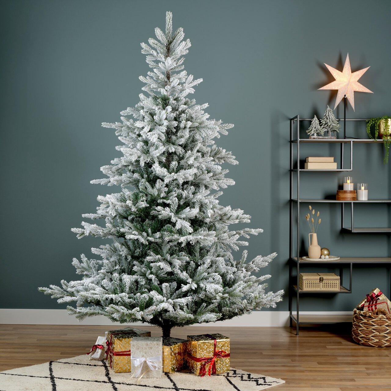 Künstlicher Weihnachtsbaum mit Schnee-Effekt, D.132 H.180 cm, frontal fotografiert, umgeben von Geschenken und weihnachtlicher Dekoration.