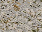Nahaufnahme eines Designer-Teppichs mit abstraktem Muster in Weiß, Grün und Braun auf grauem Hintergrund, von schräg oben fotografiert.