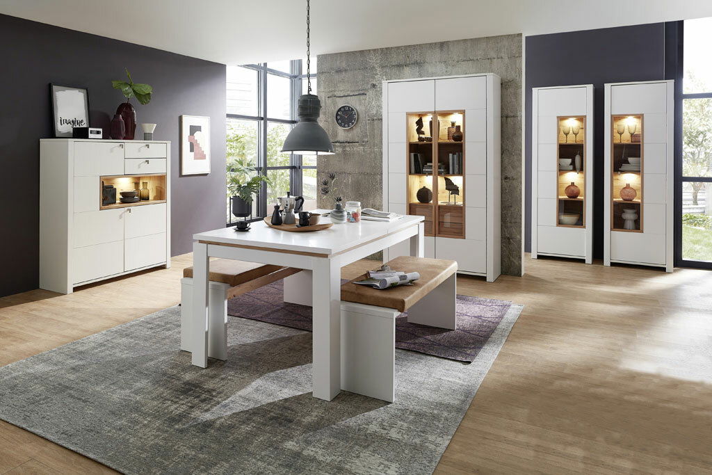 Moderne Esszimmermöbel in einem hellen Raum mit einem großen Esstisch, einer Bank und mehreren Vitrinen, seitliche Perspektive.