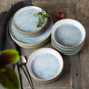 Vogelperspektive auf ein Geschirrset mit blauen Tellern und Schalen, dekoriert mit einem Basilikumzweig auf einem rustikalen Holztisch.