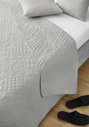 Graue Tagesdecke Nancy 220x250cm mit detailliertem Muster, auf einem Bett drapiert, aus der Vogelperspektive fotografiert.