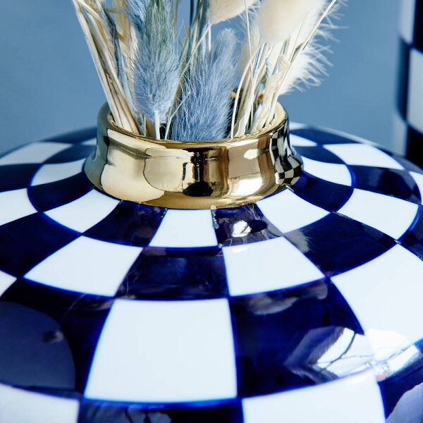 Nahaufnahme einer handbemalten Vase Harlekin mit blau-weißem Schachbrettmuster und goldener Öffnung, gefüllt mit Trockenblumen.