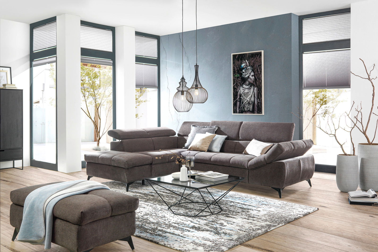 Ecksofa in modernem Wohnzimmer, Perspektive von vorne links, mit grauem Stoffbezug, dekorativen Kissen und einem passenden Hocker.