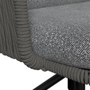 Detailaufnahme eines grauen Polsterkissens mit strukturierter Oberfläche und umlaufender, geflochtener Kordel an einem Rattan-/Geflechtmöbel, perspektivisch schräg von oben auf die Sitzkante