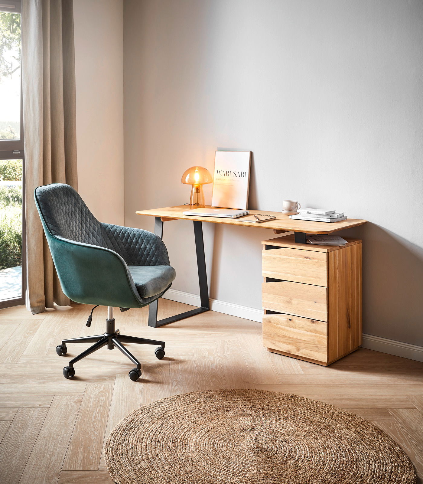 Moderner Schreibtisch aus Holz mit schwarzem Metallgestell, seitlich von einem grünen Bürostuhl und einer kleinen Lampe auf der Tischplatte begleitet, aus seitlicher Perspektive fotografiert.
