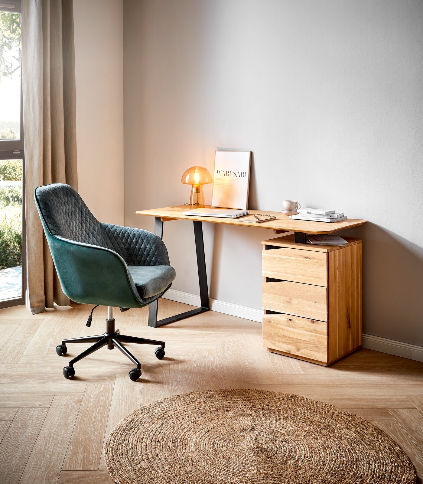 Moderner Schreibtisch aus Holz mit schwarzem Metallgestell, seitlich von einem grünen Bürostuhl und einer kleinen Lampe auf der Tischplatte begleitet, aus seitlicher Perspektive fotografiert.