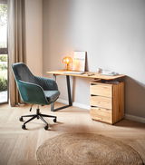 Moderner Schreibtisch aus Holz mit schwarzem Metallgestell, seitlich von einem grünen Bürostuhl und einer kleinen Lampe auf der Tischplatte begleitet, aus seitlicher Perspektive fotografiert.