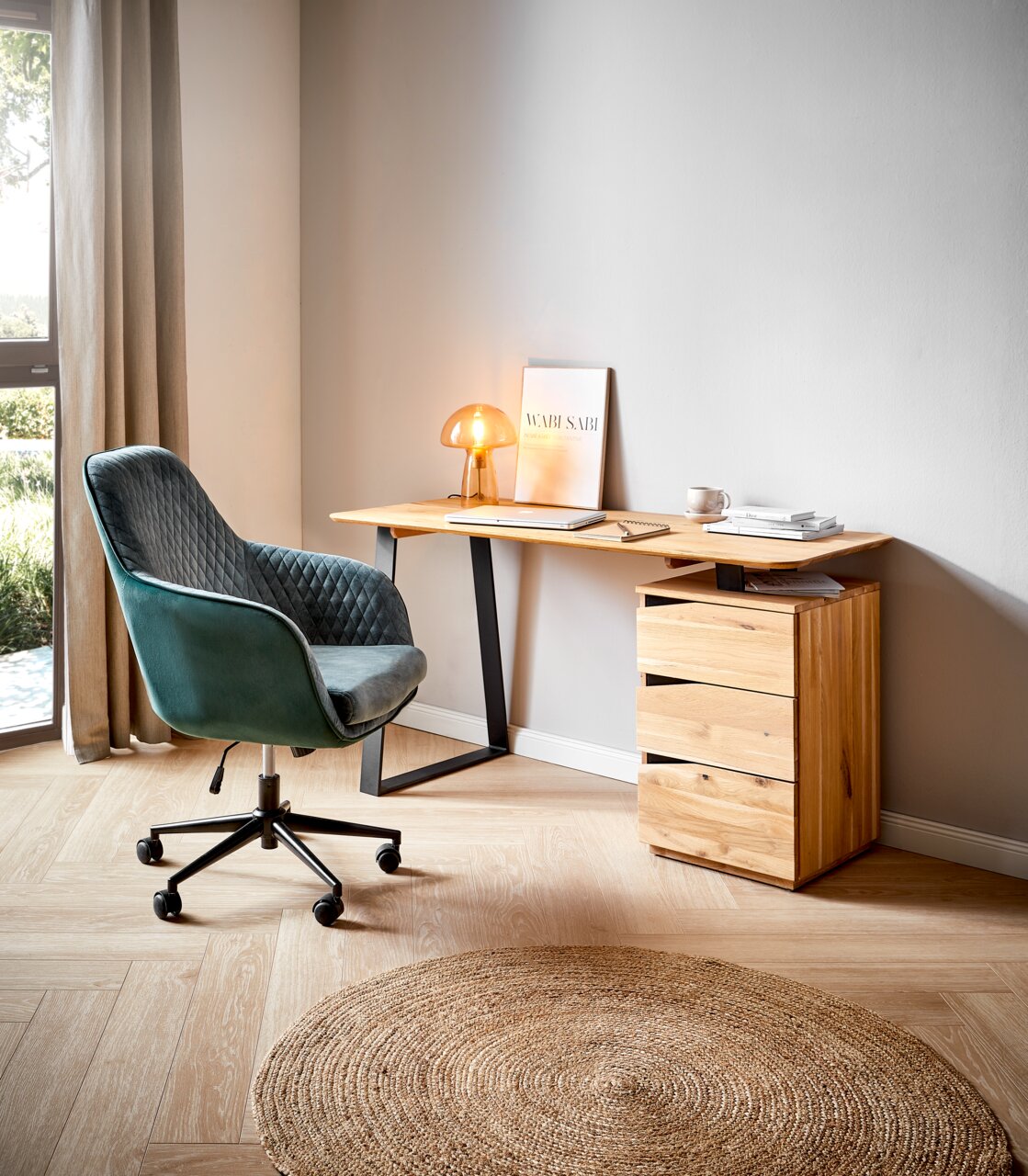 Modern houten bureau met een zwart metalen onderstel, met aan de zijkant een groene bureaustoel en een kleine lamp op het tafelblad, gefotografeerd vanuit een zijaanzicht.