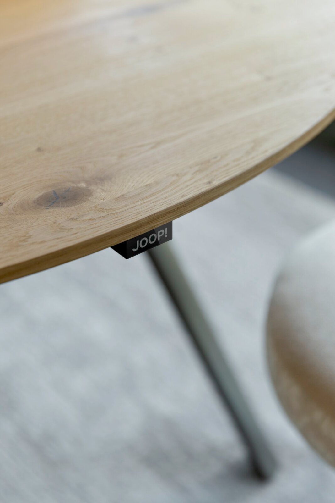 Nahaufnahme einer runden Tischplatte aus hellem Holz mit sichtbarer Maserung und JOOP!-Label an der Unterseite, schräg von oben fotografiert