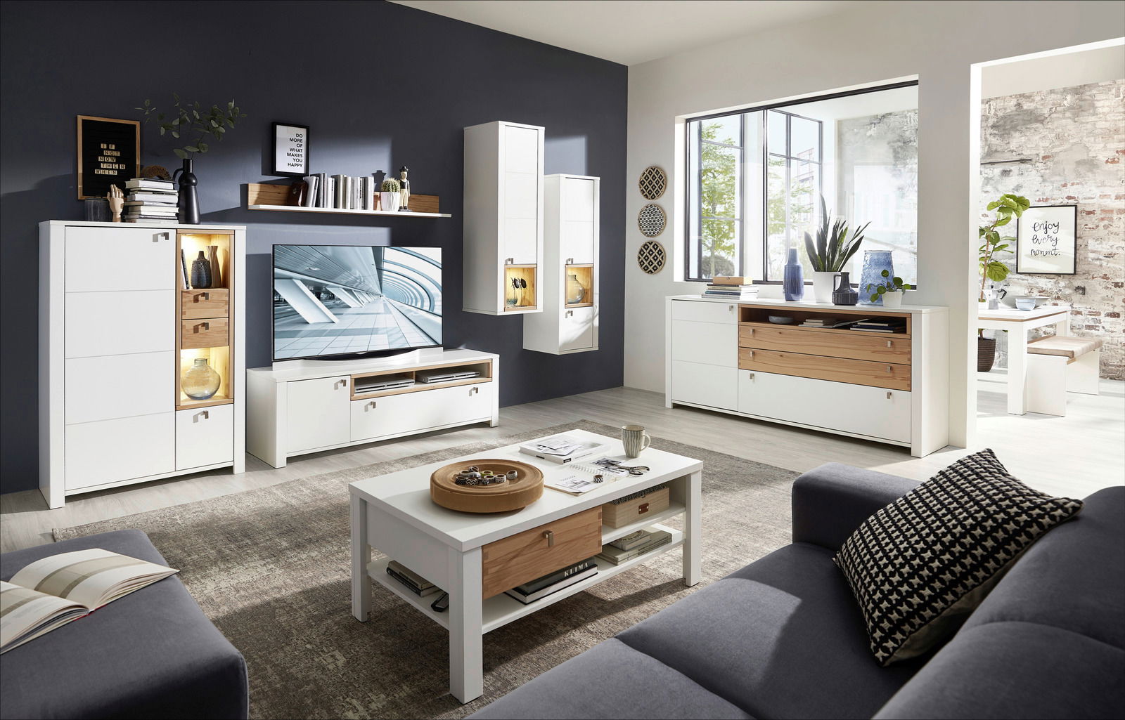 Moderne Wohnzimmermöbel in Weiß und Holzoptik, bestehend aus Couchtisch, TV-Unterteil, Hängevitrinen und Sideboard, aus der Perspektive eines gemütlichen Wohnzimmers mit Sofa.