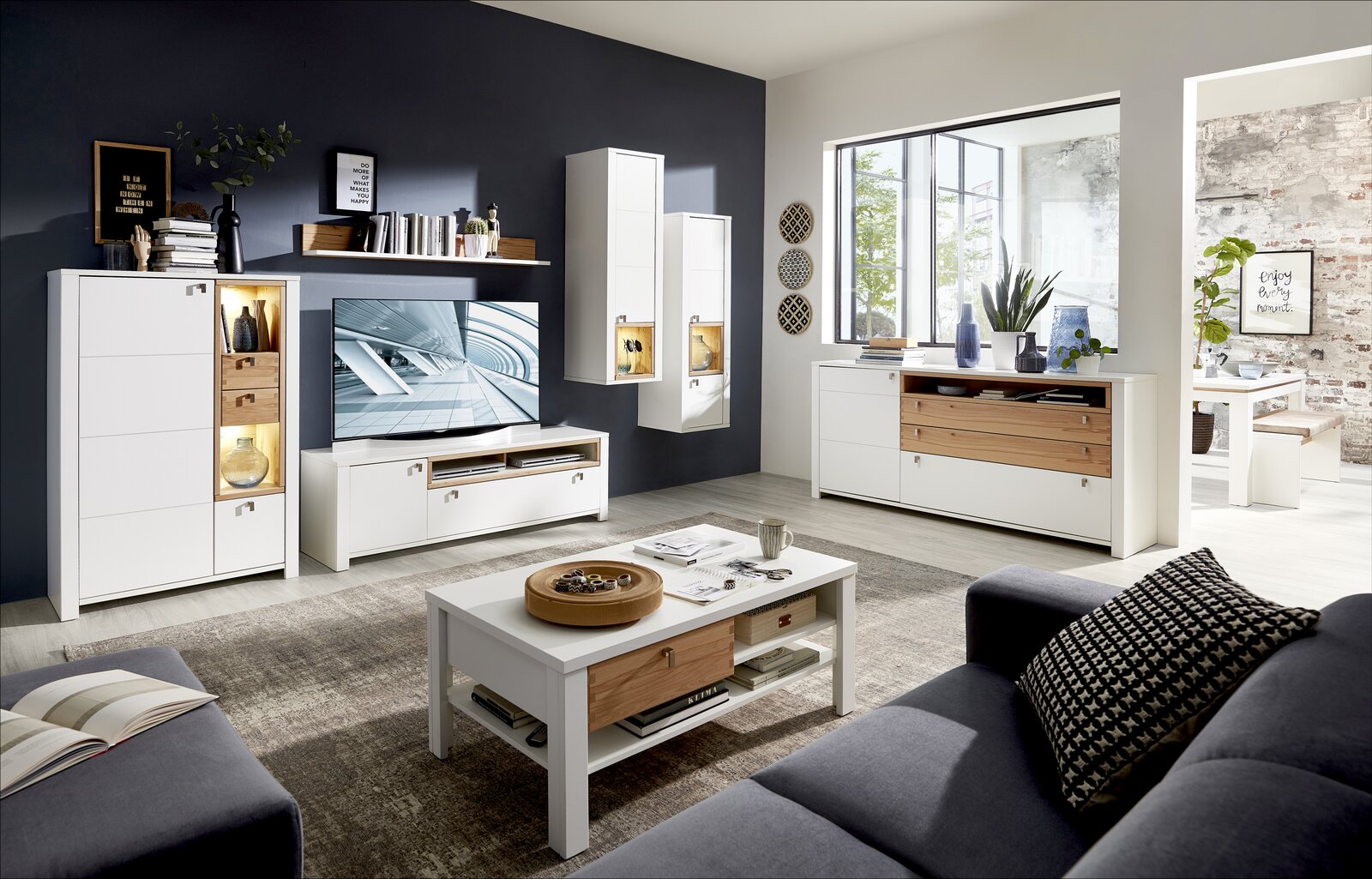 Moderne Wohnzimmermöbel in Weiß und Holzoptik, bestehend aus Couchtisch, TV-Unterteil, Hängevitrinen und Sideboard, aus der Perspektive eines gemütlichen Wohnzimmers mit Sofa.