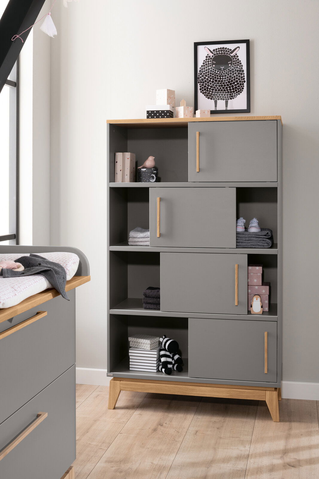 Paidi Regal STEN Graues Regal mit Holzakzenten, dekoriert mit Spielzeug und Boxen, aus frontaler Perspektive.