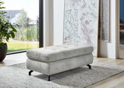 Grauer XXL-Hocker mit schwarzem Metallgestell in einem modernen Wohnzimmer, seitliche Perspektive.