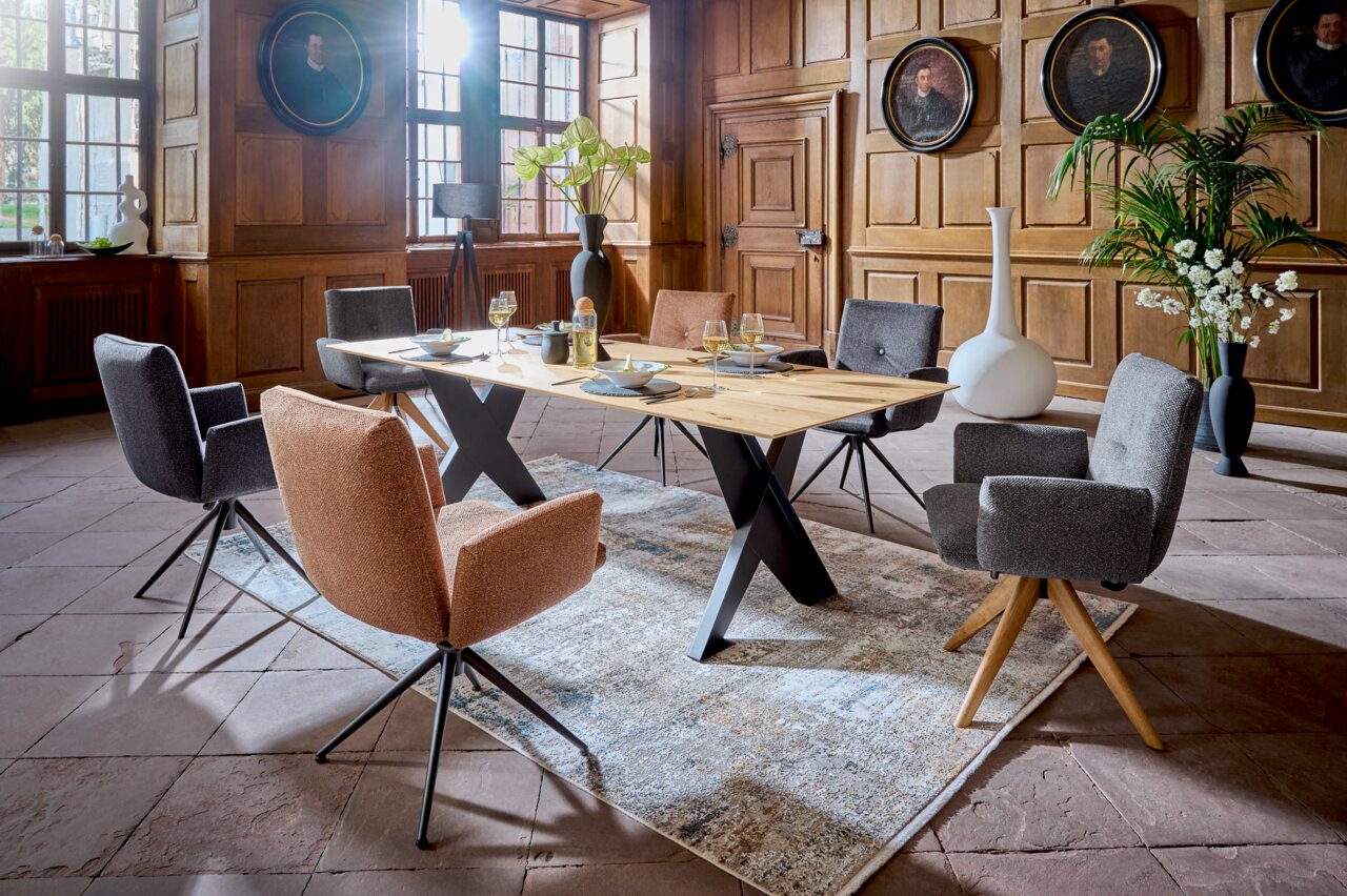 Moderner Esstisch 220x100 cm mit X-förmigen Beinen in einem eleganten Raum mit Holzwänden, umgeben von stilvollen Stühlen. Perspektive: seitlich.