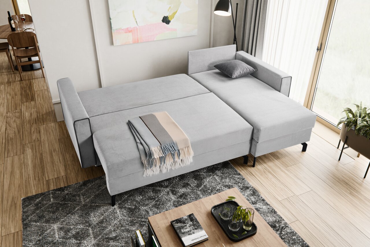 Graues Schlafsofa in L-Form von oben fotografiert, mit einer Decke und einem Kissen dekoriert, in einem modernen Wohnzimmer mit Holzboden und großen Fenstern.