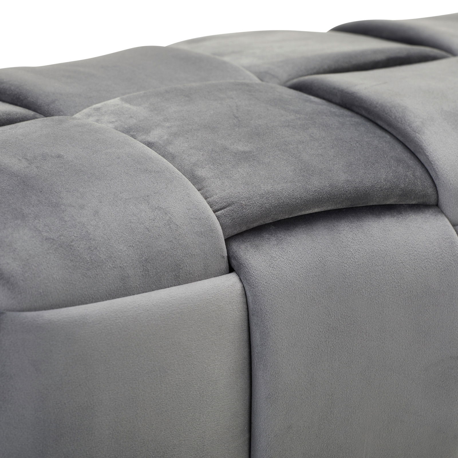 Nahaufnahme einer grauen, gepolsterten Hockerbank mit weicher, samtartiger Oberfläche und quadratischem Muster, seitliche Perspektive.