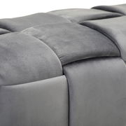 Nahaufnahme einer grauen, gepolsterten Hockerbank mit weicher, samtartiger Oberfläche und quadratischem Muster, seitliche Perspektive.