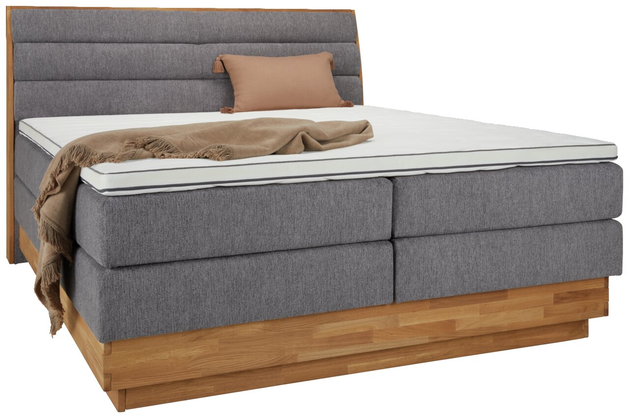 Z2 Boxspringbett MARISSA Boxspringbett MARISSA in grauem Stoff mit Holzrahmen, seitliche Perspektive, dekoriert mit einem braunen Kissen und einer Decke.