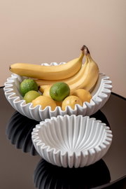 Zwei weiße, geriffelte Schalen auf einem Tisch, gefüllt mit Bananen, Limetten und Zitronen. Die Perspektive ist von oben leicht seitlich.