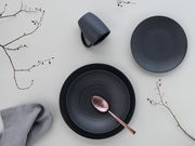 Draufsicht auf ein elegantes, dunkelgraues Kombiservice-Set mit Teller, Tasse und Löffel, dekoriert mit Zweigen und Stoffserviette.