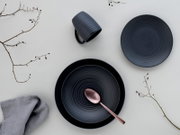 Draufsicht auf ein elegantes, dunkelgraues Kombiservice-Set mit Teller, Tasse und Löffel, dekoriert mit Zweigen und Stoffserviette.